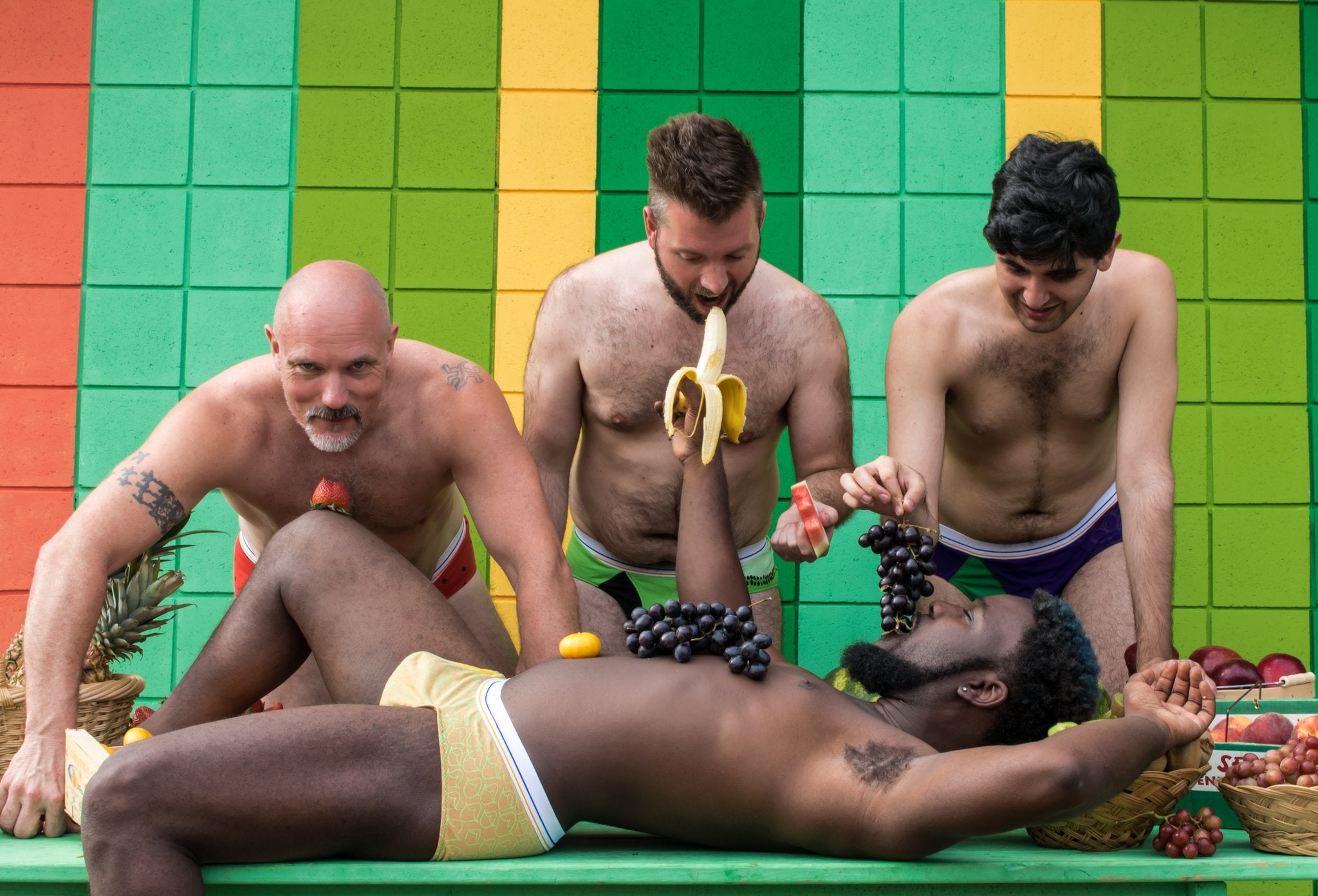 4 men in undies decorated with fruit eating fruit